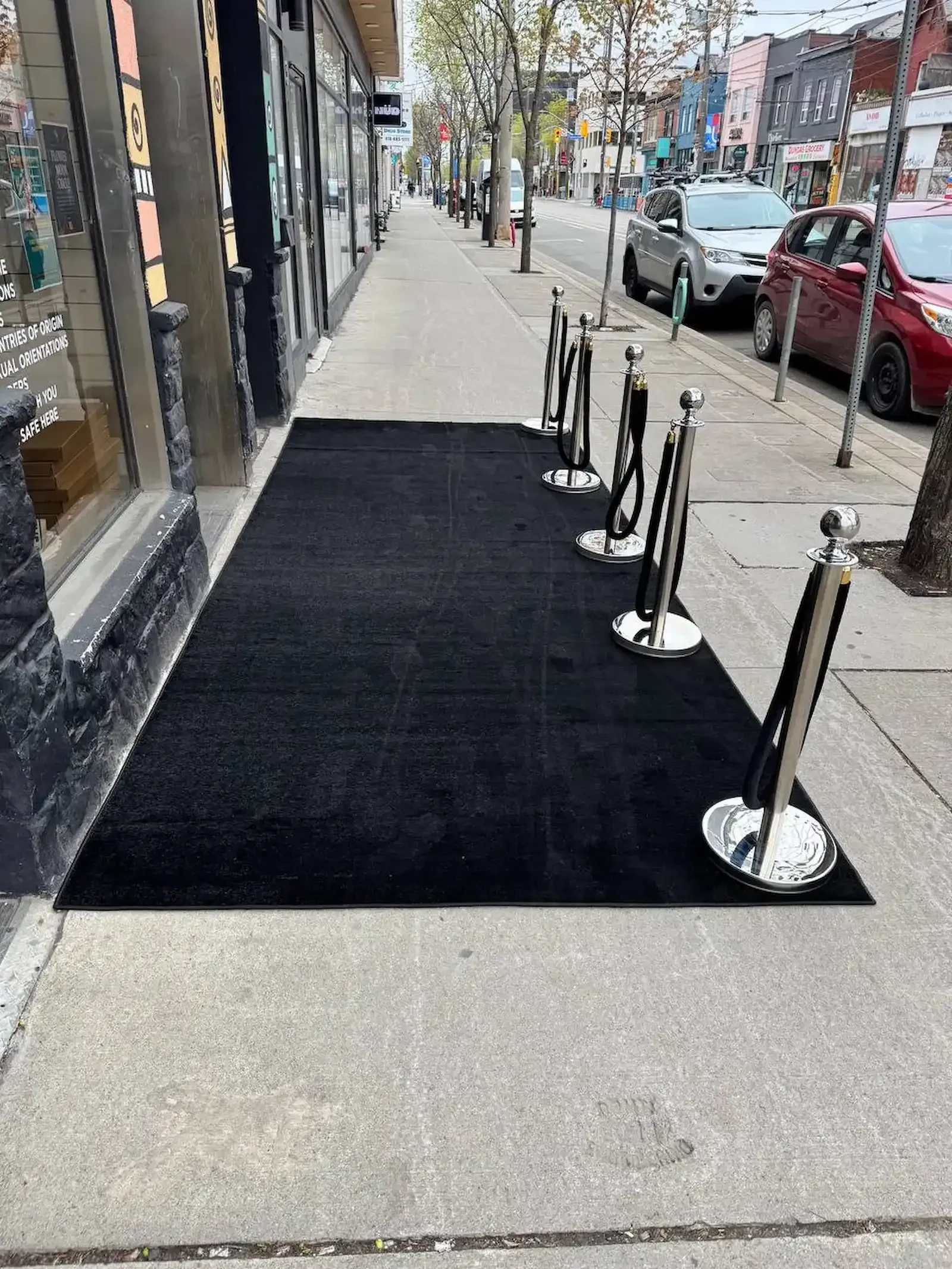 Black carpet runner outdoors, edged with polished chrome rope stanchions and black velvet ropes